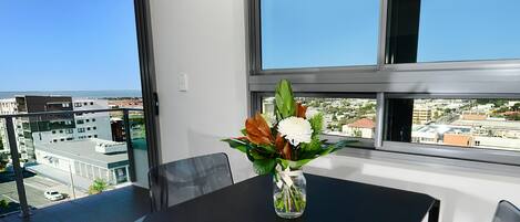 Un balcón con una mesa y sillas, un jarrón con flores y vistas a la ciudad.