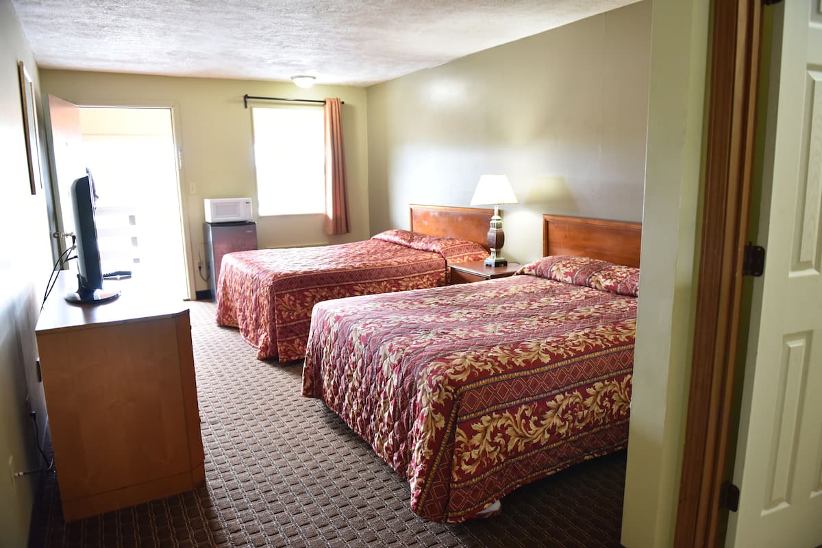 A hotel room with two beds, a desk, a television, and a window with curtains.