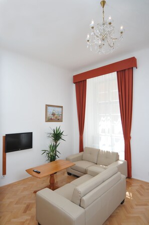 A living room with a sectional sofa, a wooden coffee table, a potted plant, a flat-screen TV, and a chandelier. - Apartment house Anenská (Prague)