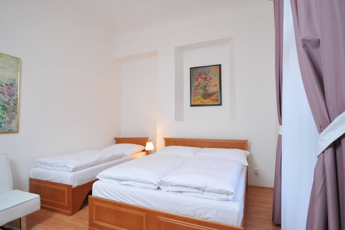 A hotel room with two single beds, a bedside table, a chair, and a painting on the wall.