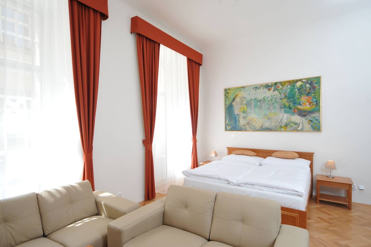 A hotel room with a bed, two bedside tables, a sofa, and a painting on the wall.