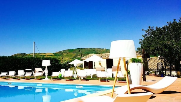A poolside area with lounge chairs and umbrellas, a clear blue sky, and a view of hills in the background. - Agriturismo Casalicchio (Cammarata)