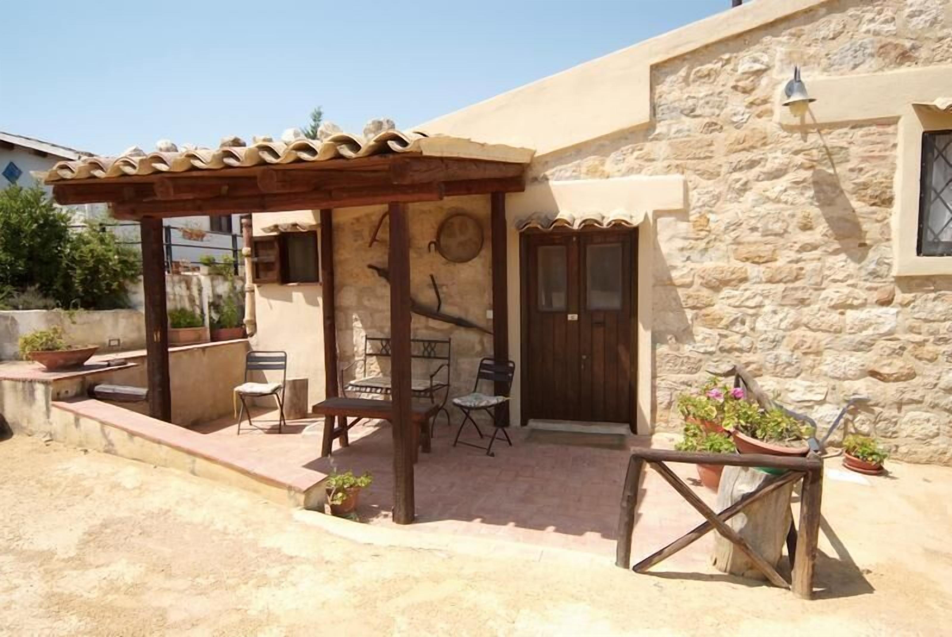 Une maison en pierre avec un patio agrémenté d’une pergola en bois, des meubles d’extérieur et des plantes en pot.