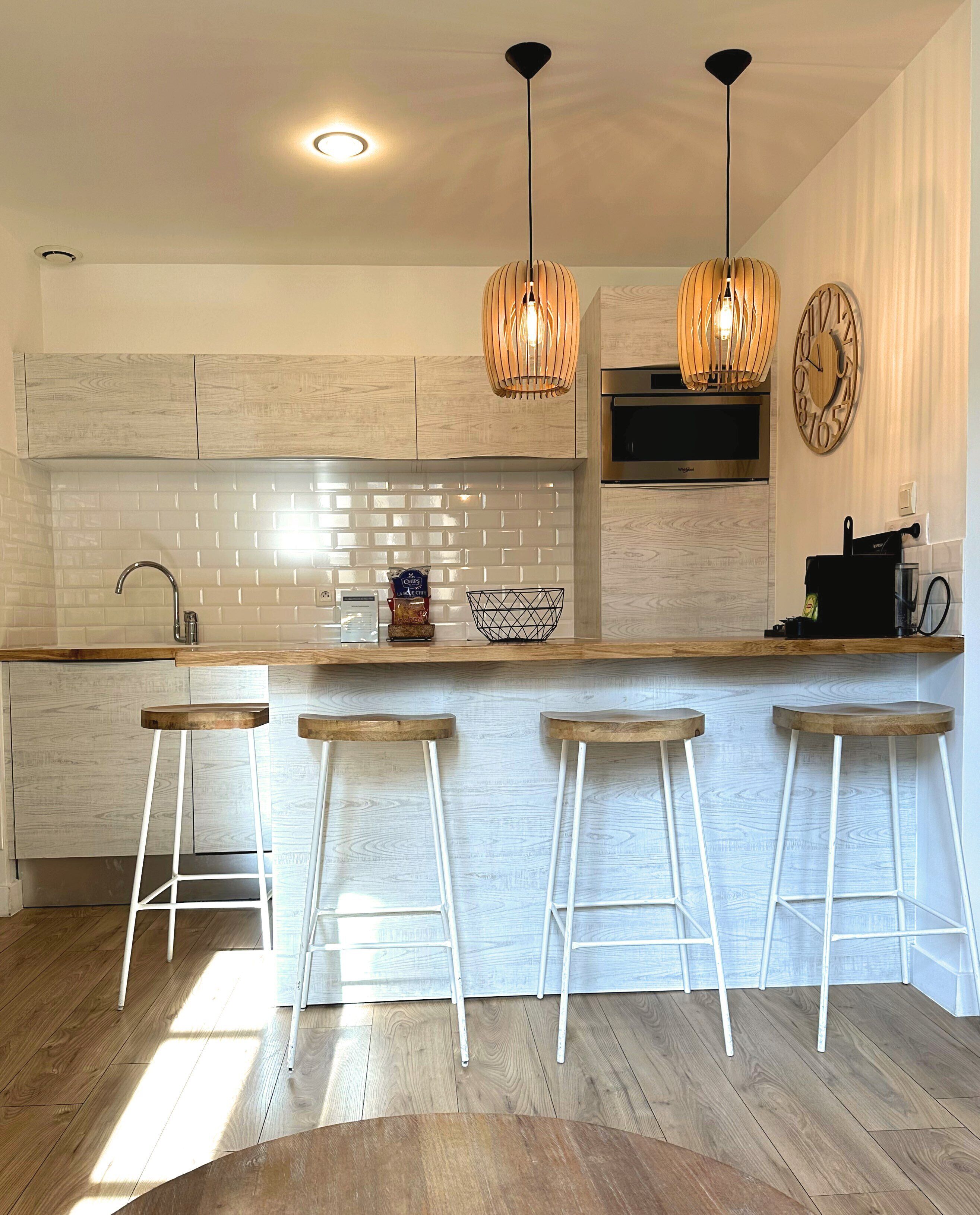 Een moderne keuken met houten kastjes, een witte betegelde achterwand en drie barstoelen.