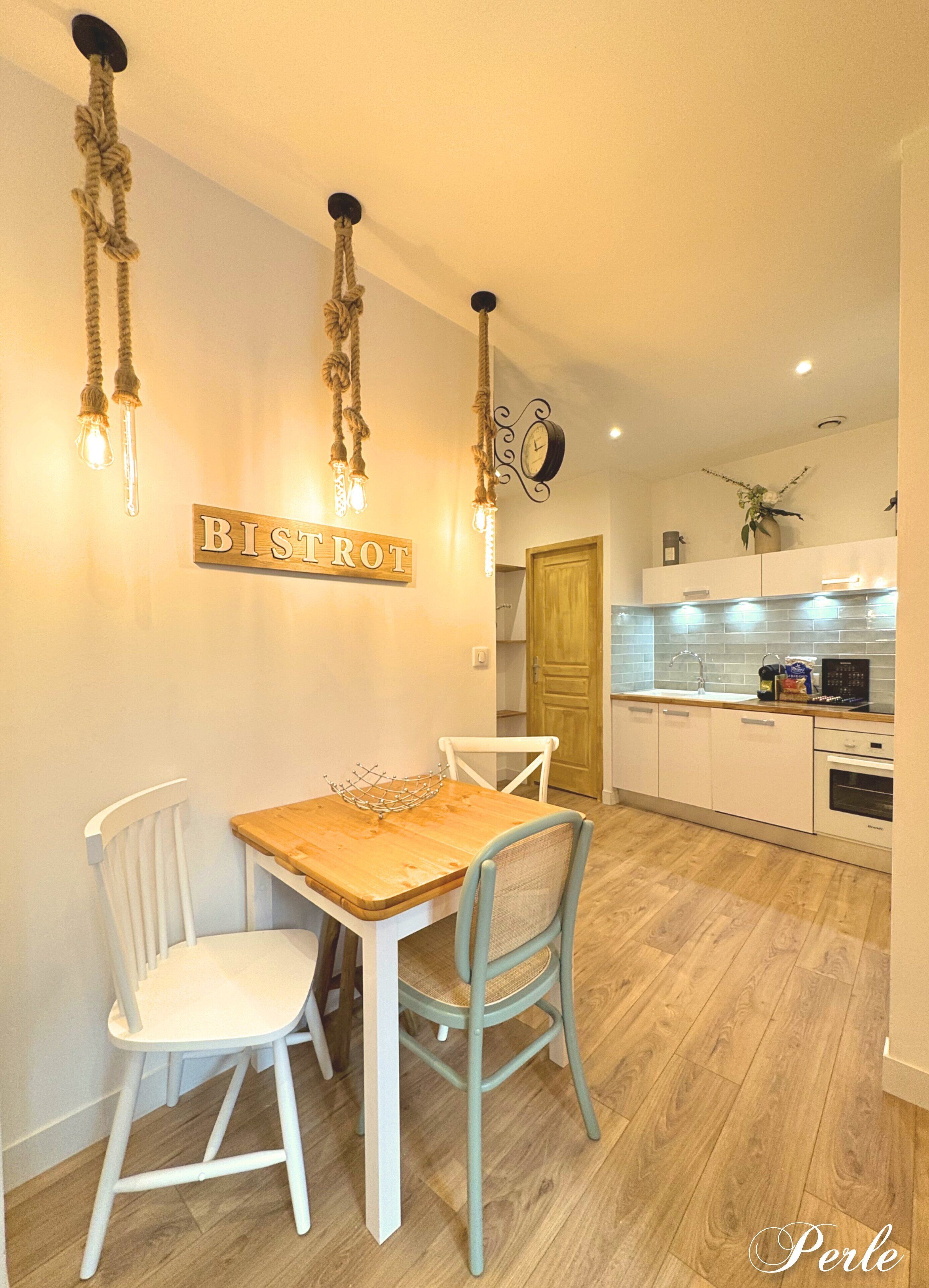 Un comedor con una mesa y sillas de madera, un letrero que dice "BISTROT" y una cocina al fondo.