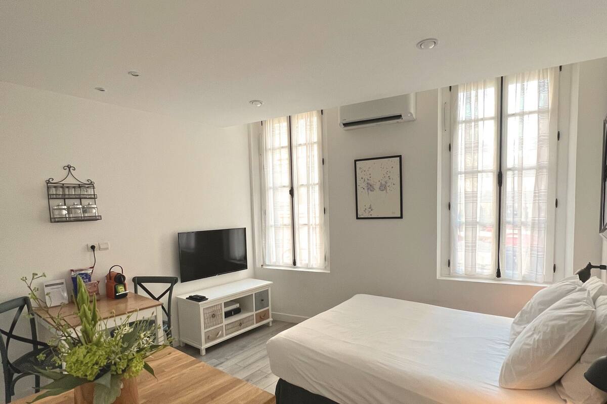 A modern bedroom with a bed, a TV, a desk, and a window.