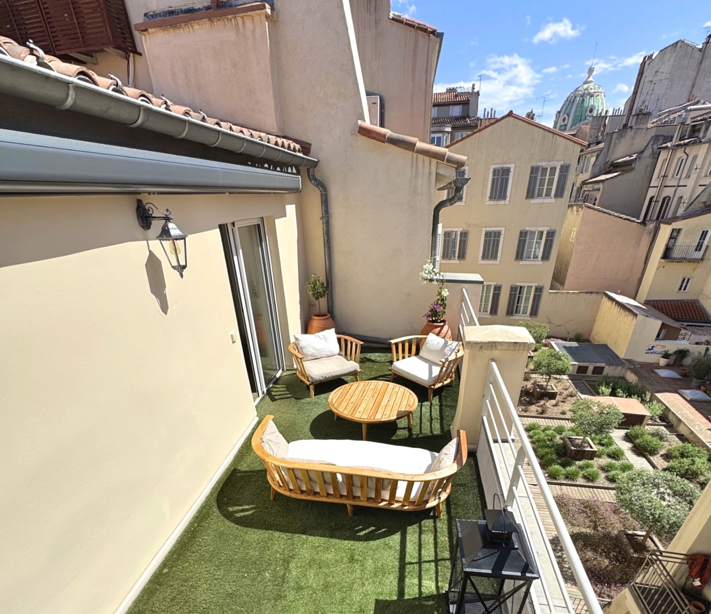 Terraço no topo do prédio com uma pequena mesa e cadeiras, uma planta em vaso e vista para a paisagem urbana.