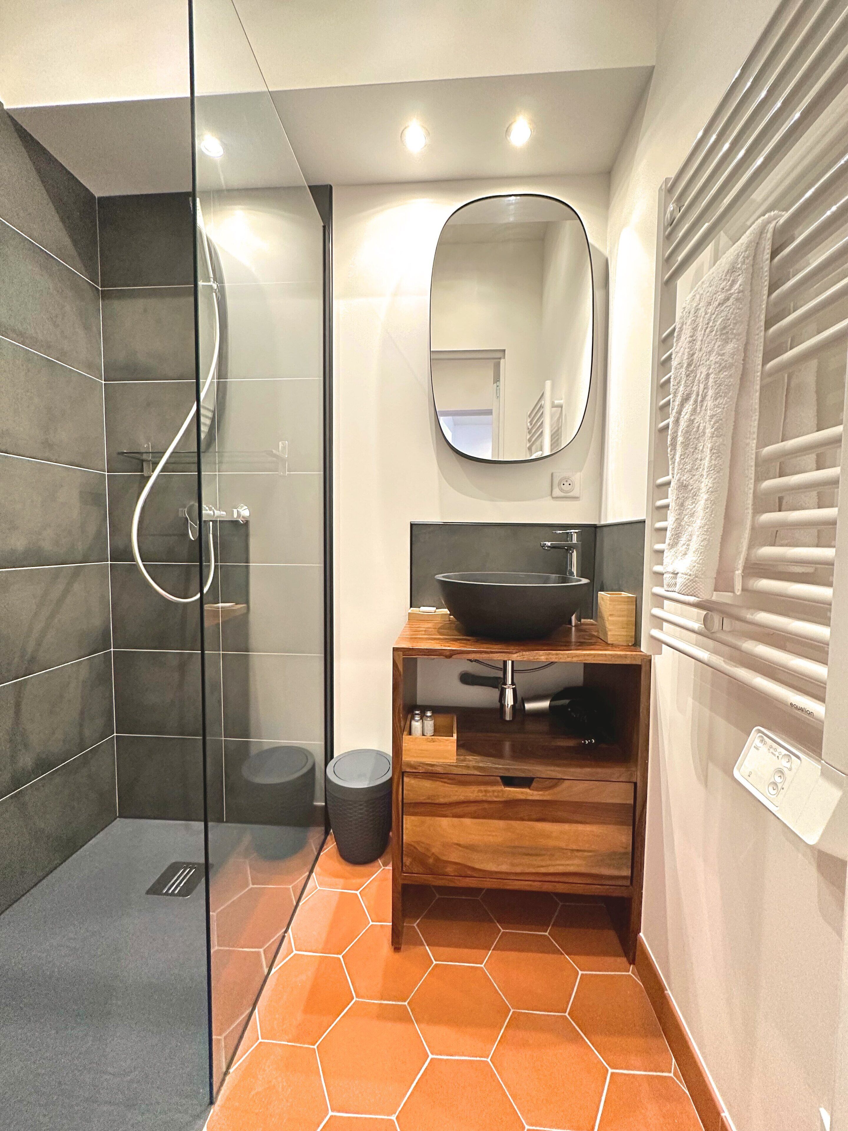 Un baño moderno con cabina de ducha de vidrio, tocador de madera con lavamanos y espejo superior.