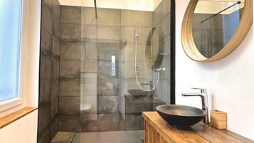 A modern bathroom with a glass-enclosed shower, a wooden vanity with a round mirror, and a hexagonal tile floor.