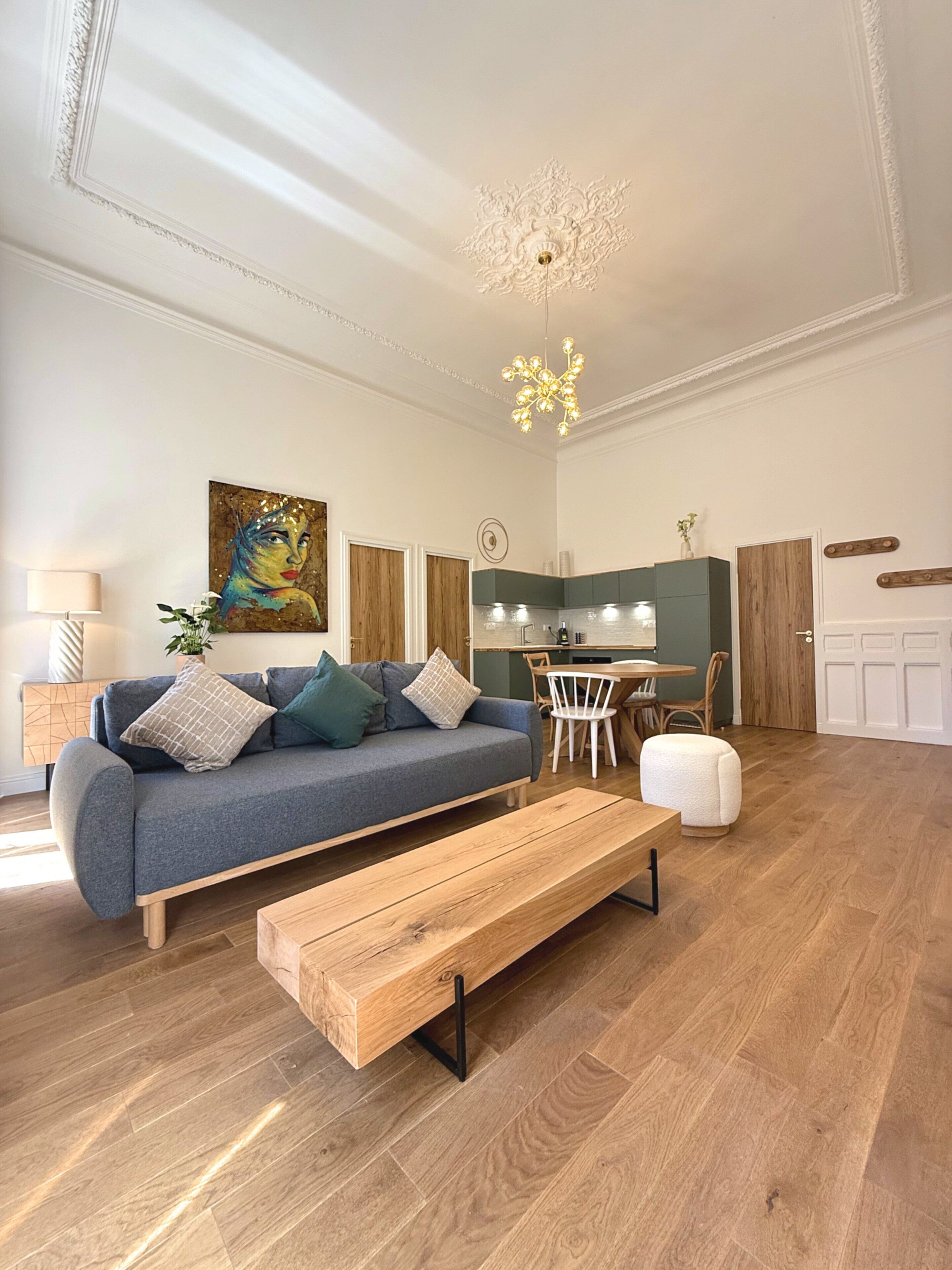 A modern living room with a sofa, a wooden bench, a dining area, and a kitchen in the background.
