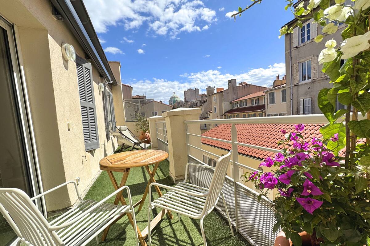 A balcony with a table and chairs, a potted plant, and a view of surrounding buildings.