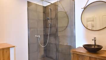 Un baño moderno con ducha envuelta en vidrio, tocador de madera y espejo redondo.