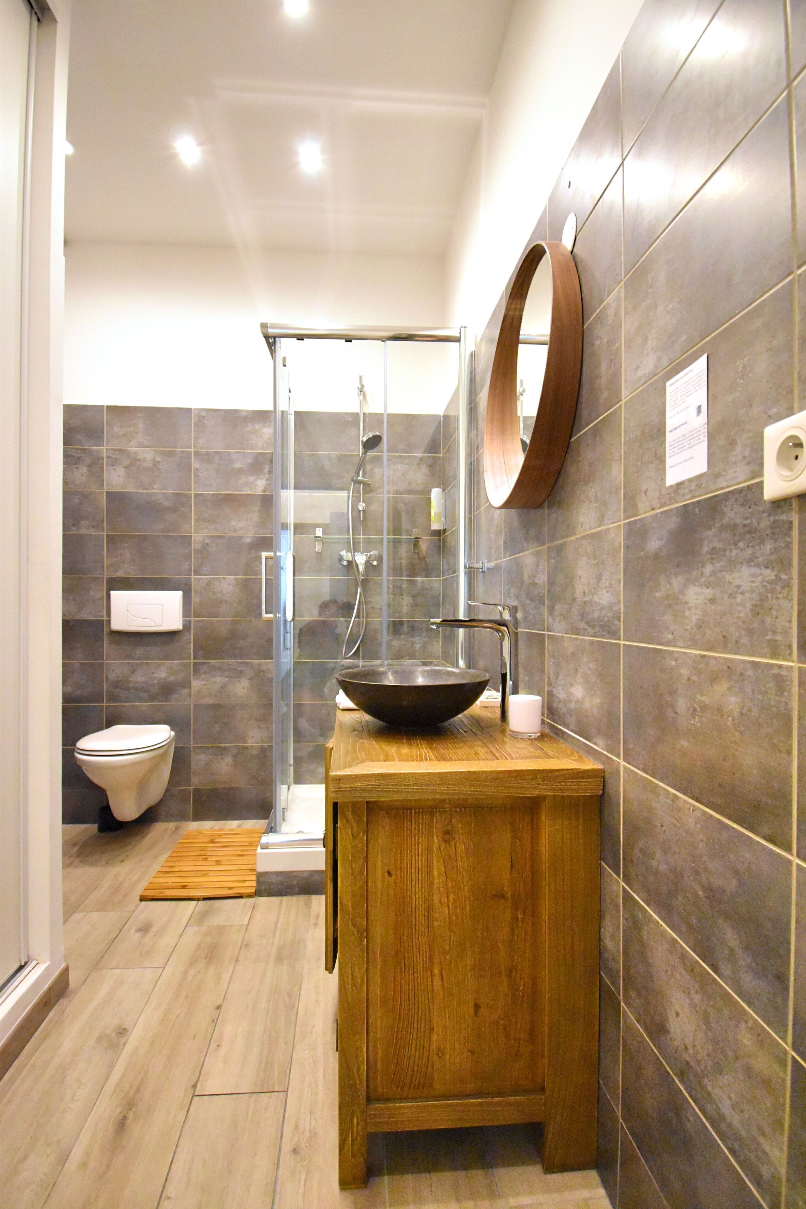 A modern bathroom with a wooden vanity, a large mirror, and a glass-enclosed shower.