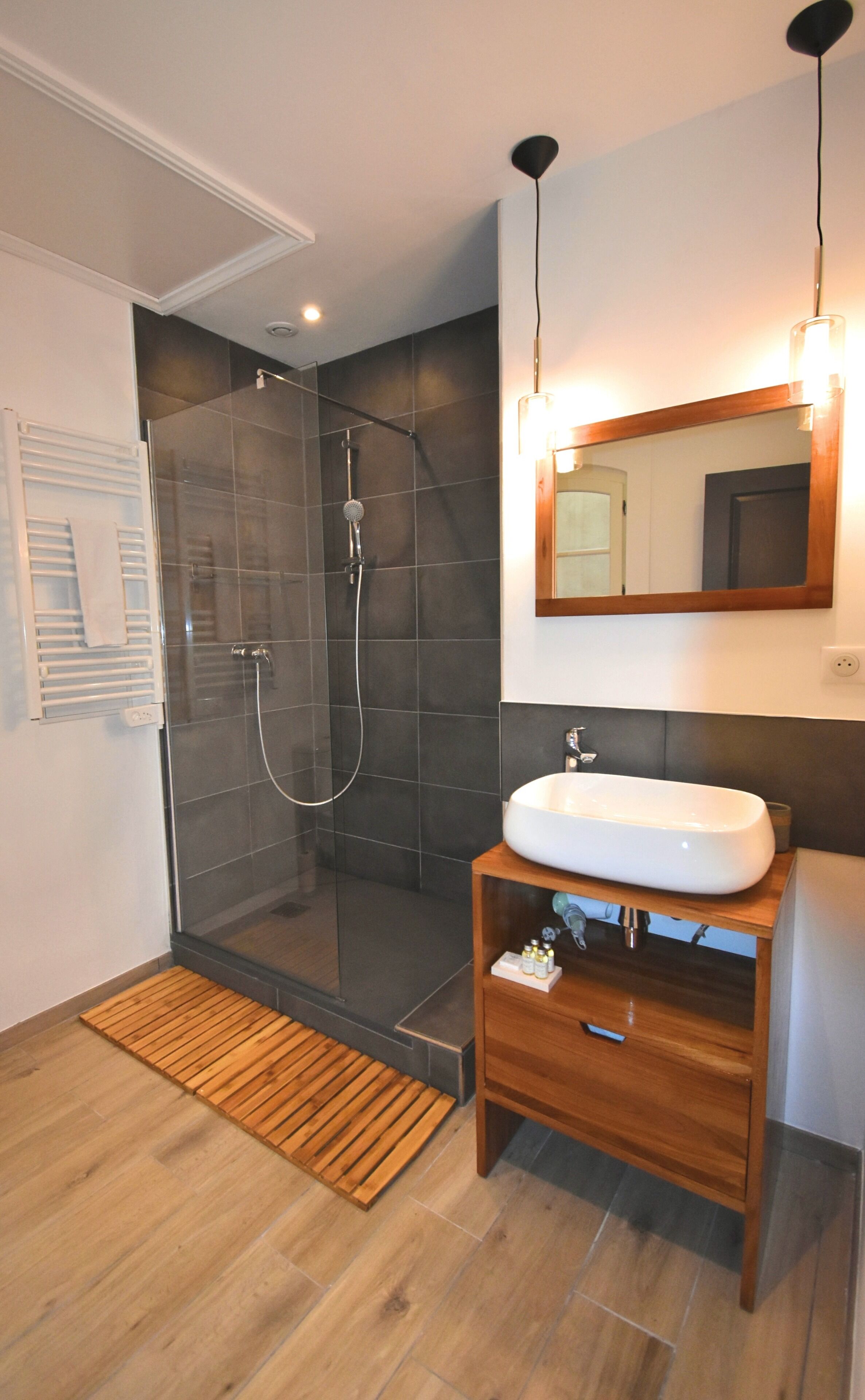 A modern bathroom with a glass-enclosed shower, a white sink, and a wooden vanity.