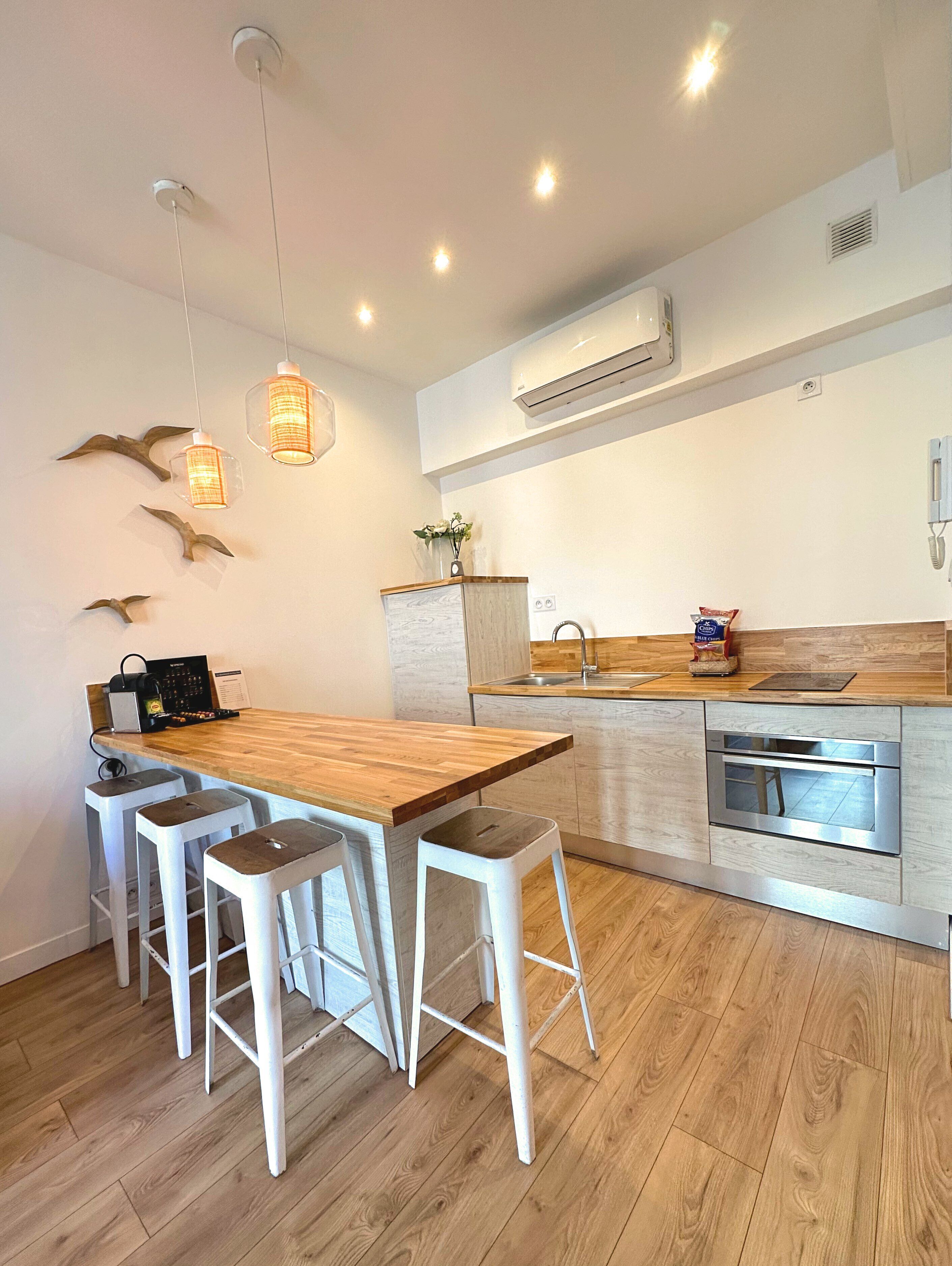 A modern kitchen with a wooden island, bar stools, and pendant lights.