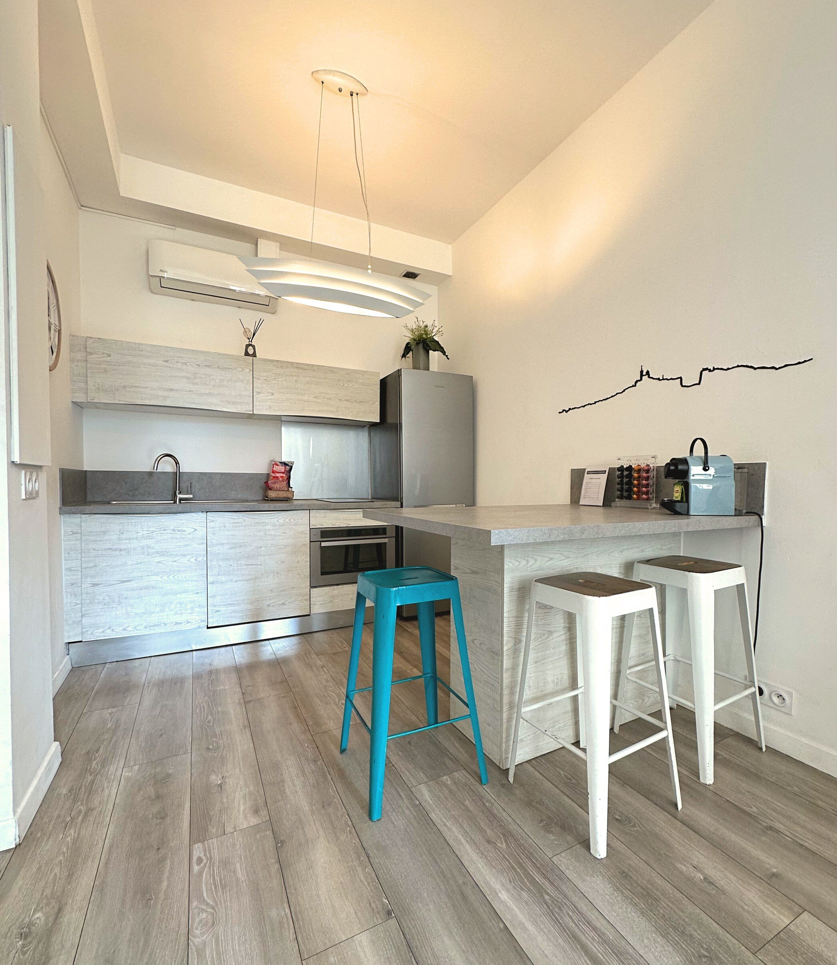 A modern kitchen with a central island, two bar stools, and a wall-mounted coffee machine.