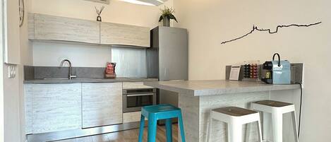 A modern kitchen with a central island, two bar stools, and a wall-mounted coffee machine.