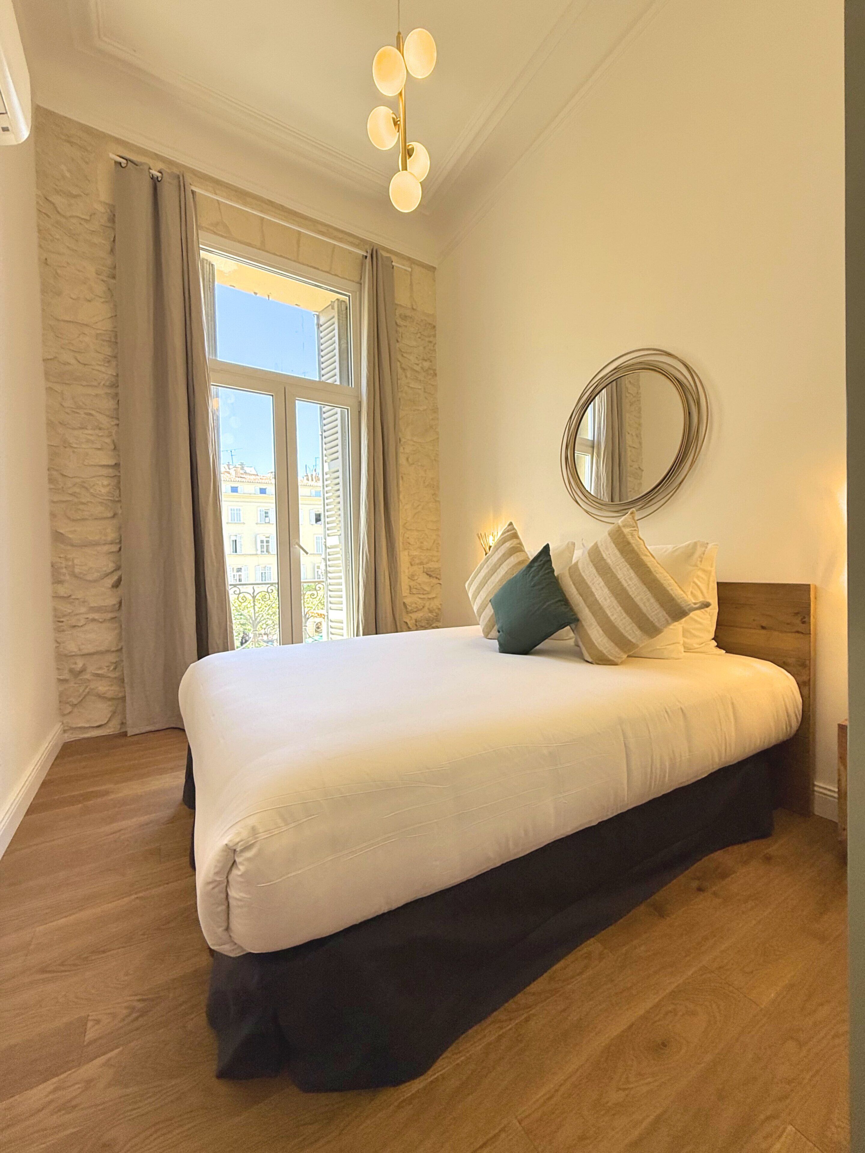 Un dormitorio con una cama grande, un espejo redondo y vistas de edificios a través de la ventana.