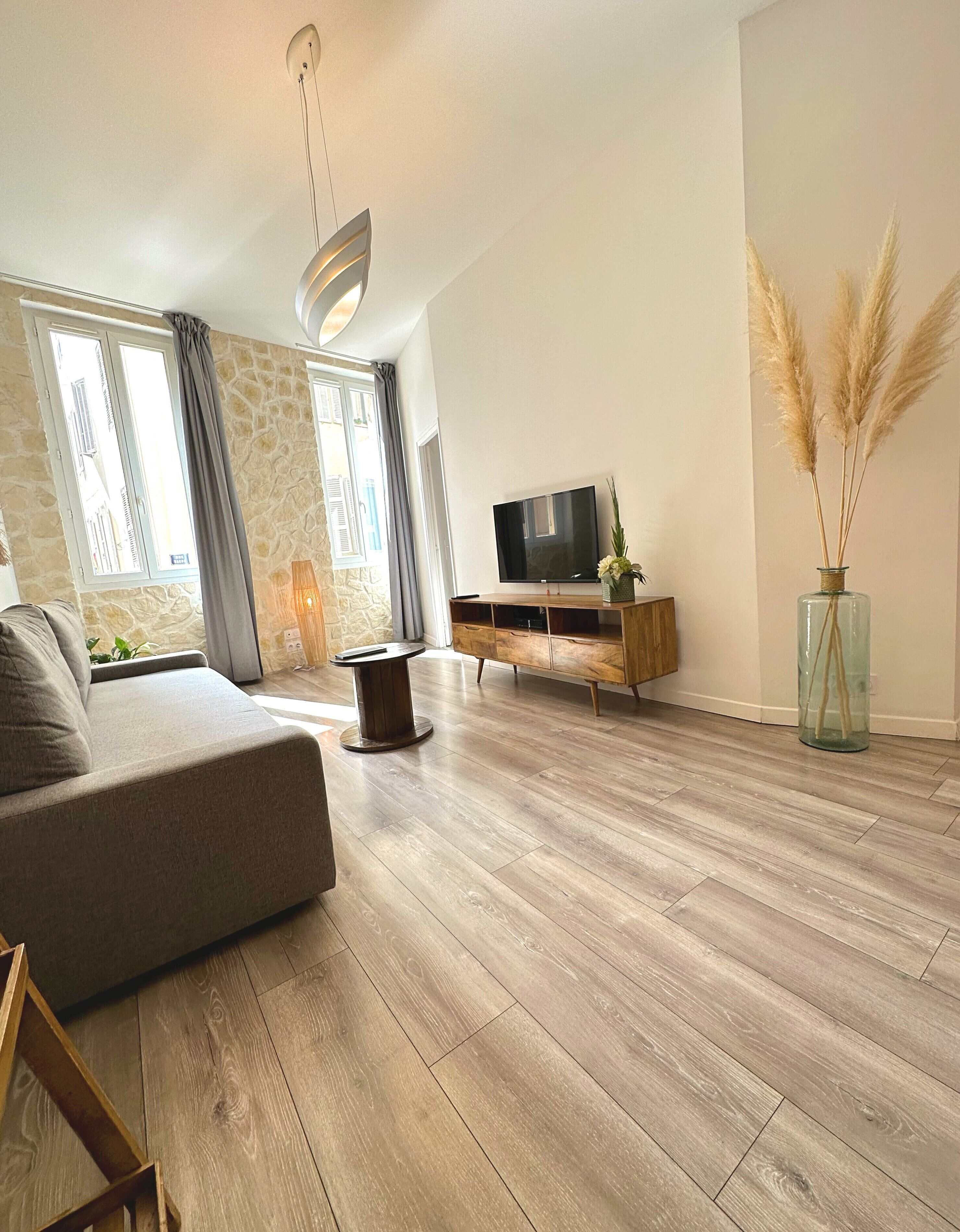 A modern living room with a grey sofa, a wooden coffee table, a flat-screen TV on a wooden stand, and a vase with pampas grass.