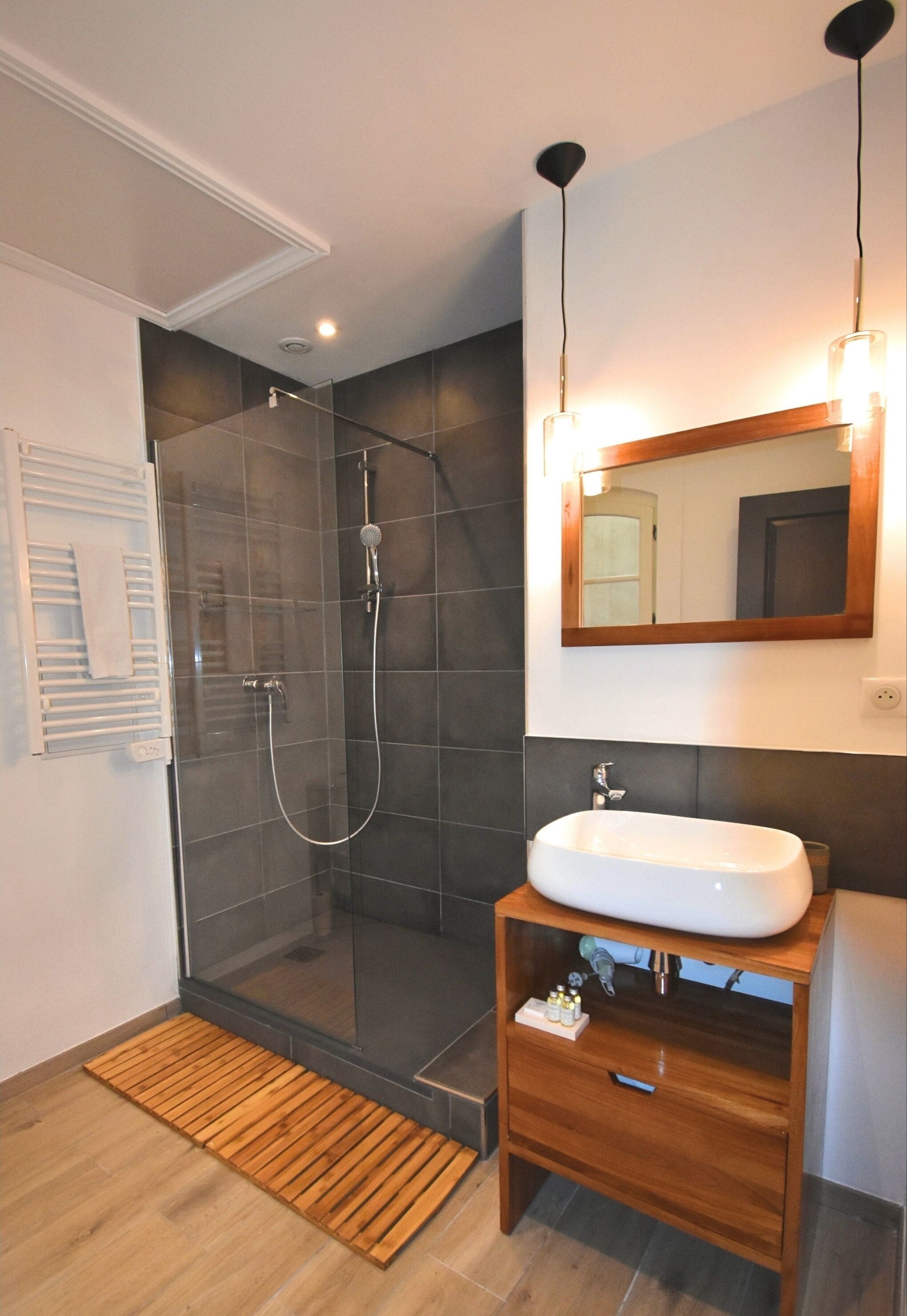 A modern bathroom with a glass-enclosed shower, a wooden vanity with a sink, and a mirror with lights.