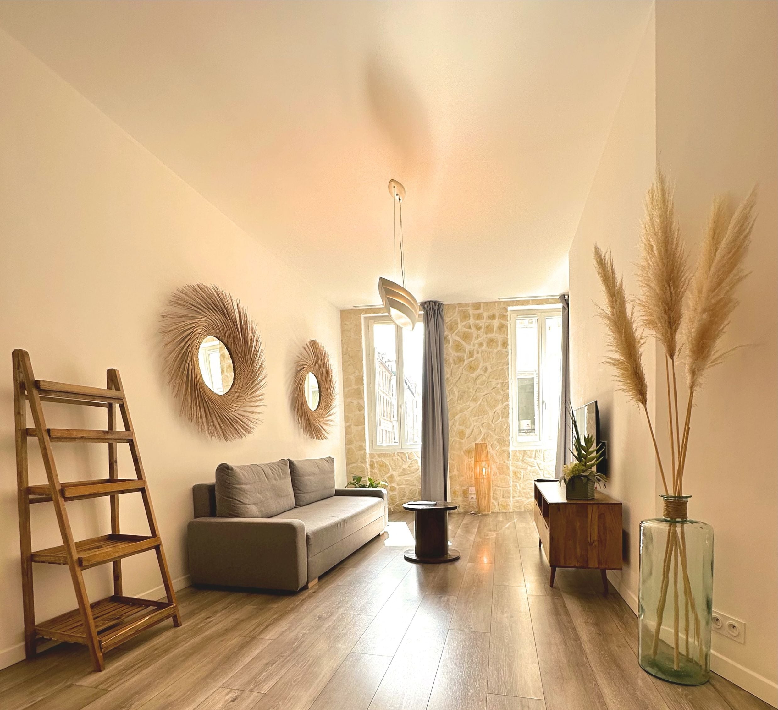 Un salon moderne avec un plancher en bois, un canapé, une échelle, des miroirs décoratifs, une cheminée et un vase contenant des plumes d'herbe des pampas.