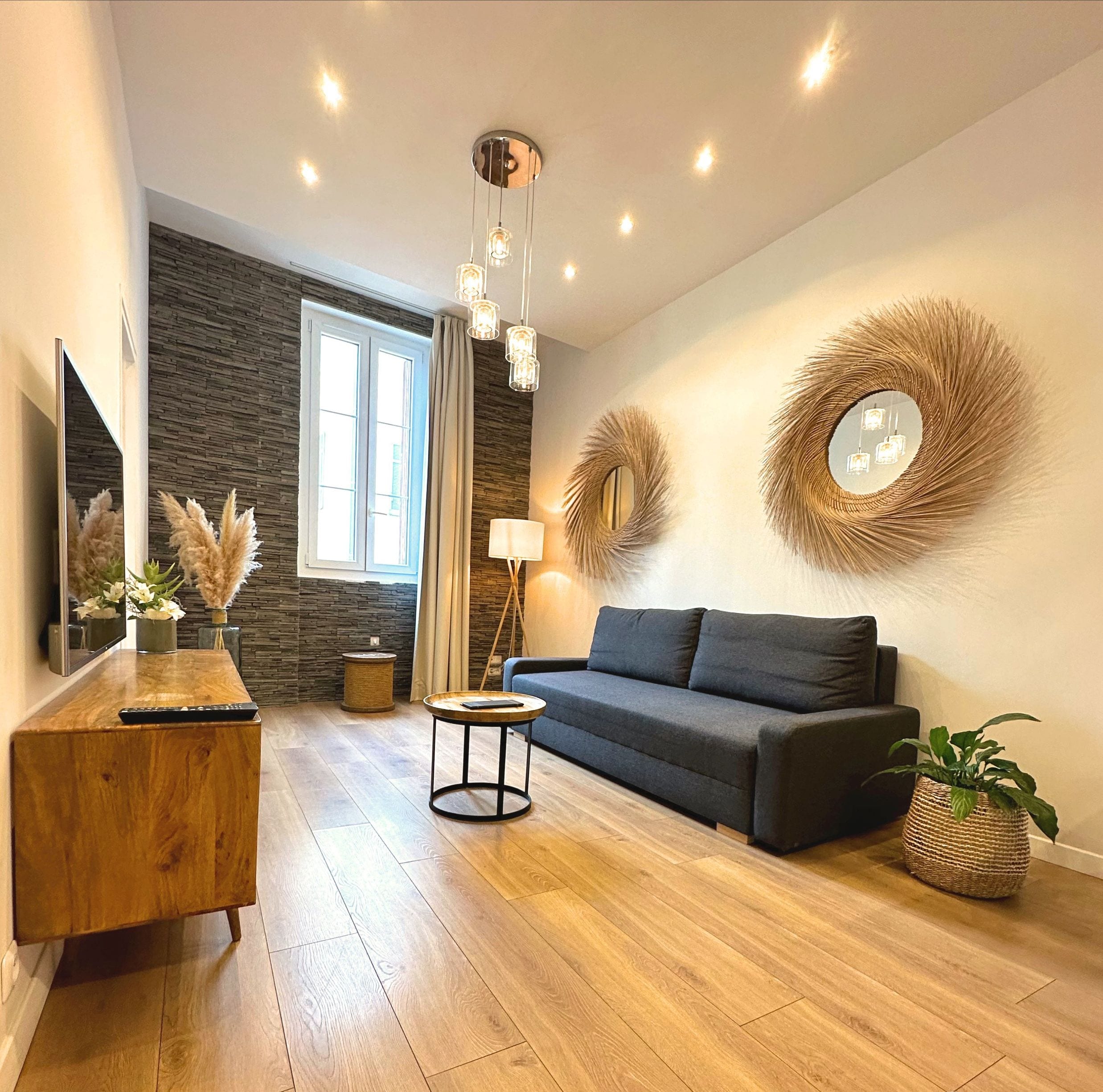 Una sala de estar moderna con suelo de madera, un sofá gris, una mesa de centro redonda y espejos decorativos en las paredes.