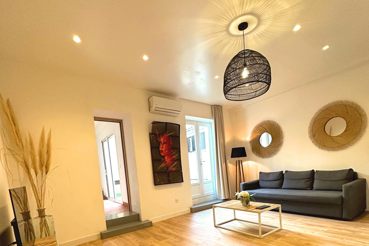 A spacious living room with a wooden floor, a grey sofa, a coffee table, and a hanging light fixture.