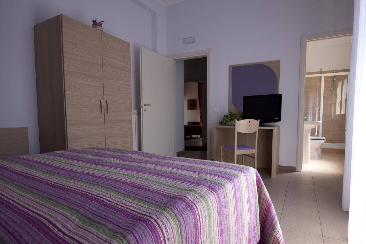 A bedroom with a bed, wardrobe, desk, TV, and bathroom visible through an open door.