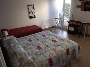 A bedroom with a large bed, a red sofa, a desk with a chair, and a window with a view of greenery.