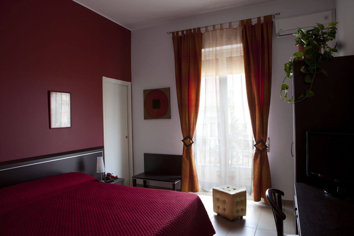 A hotel room with a bed, a desk, a chair, a TV, and a window with curtains.