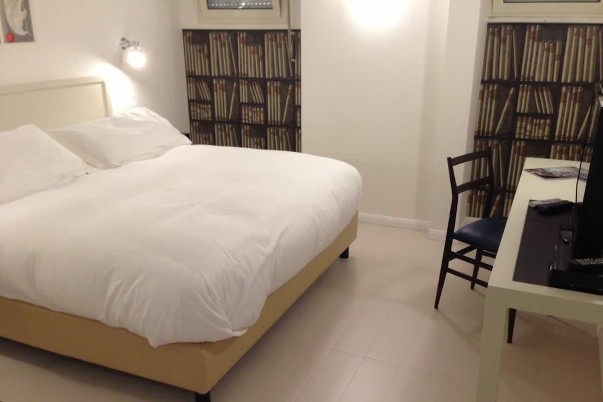 A bedroom with a bed, a desk, and a chair. There is a bookshelf against the wall.