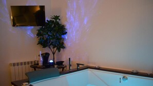 Ein modernes Badezimmer mit einer großen Badewanne, einem kleinen Tisch mit einer Pflanze und einem an der Wand montierten Fernseher.
