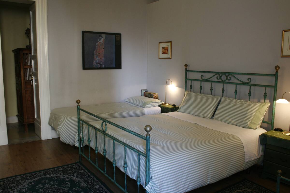 Een tweepersoonsbed met metalen frame, twee nachtkastjes en een bijzetbed met lamp.