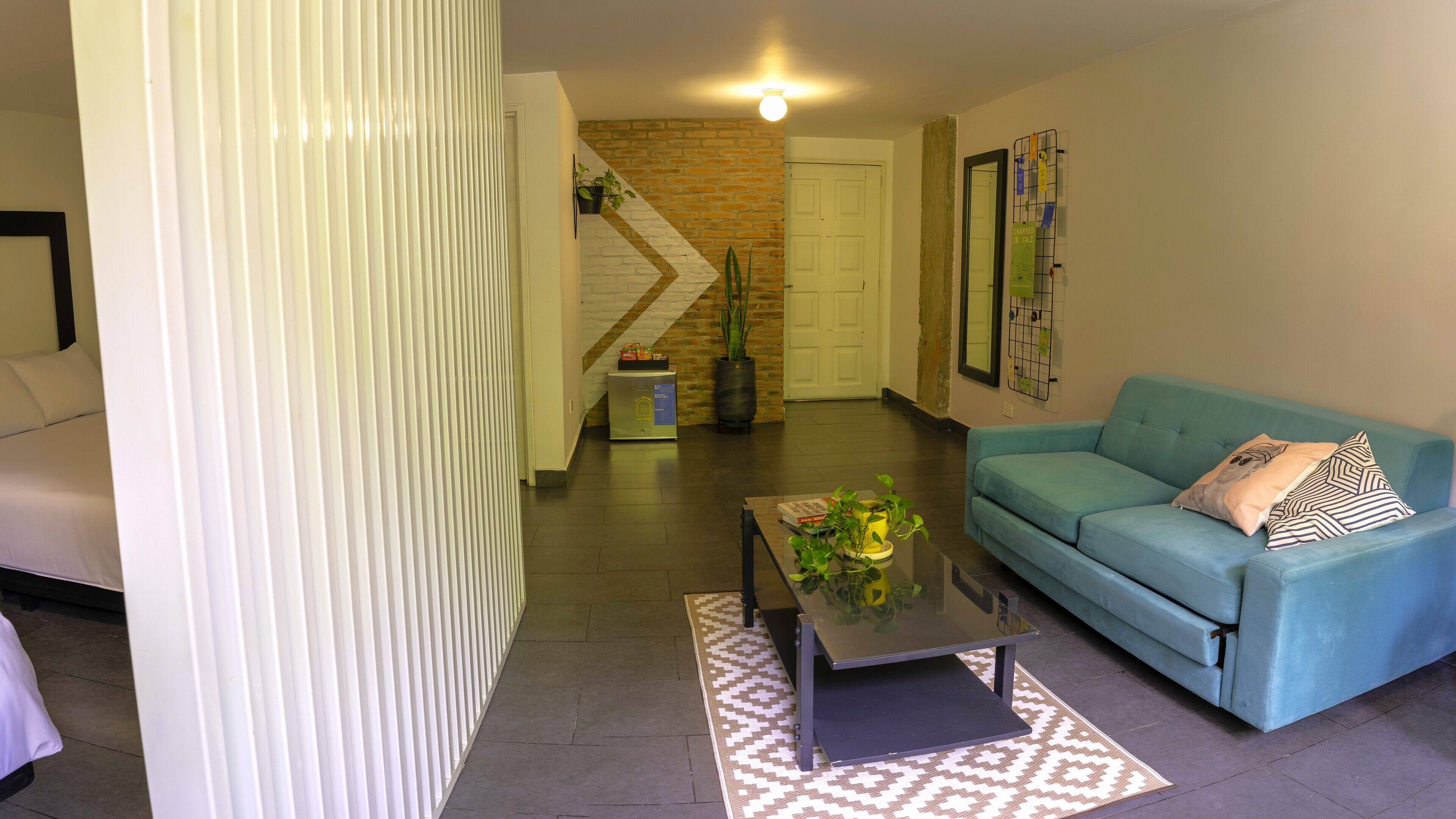 A living room with a blue sofa, a coffee table, and a patterned rug. There is a staircase with a brick wall and a door.