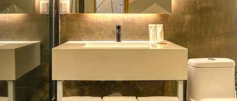 A modern bathroom with a large mirror, a white sink, and a toilet. There are towels hanging on hooks and a shower area visible.