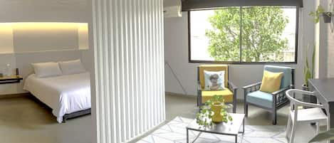 A modern hotel room with a bed, a desk, a chair, and a large window with a view of trees.
