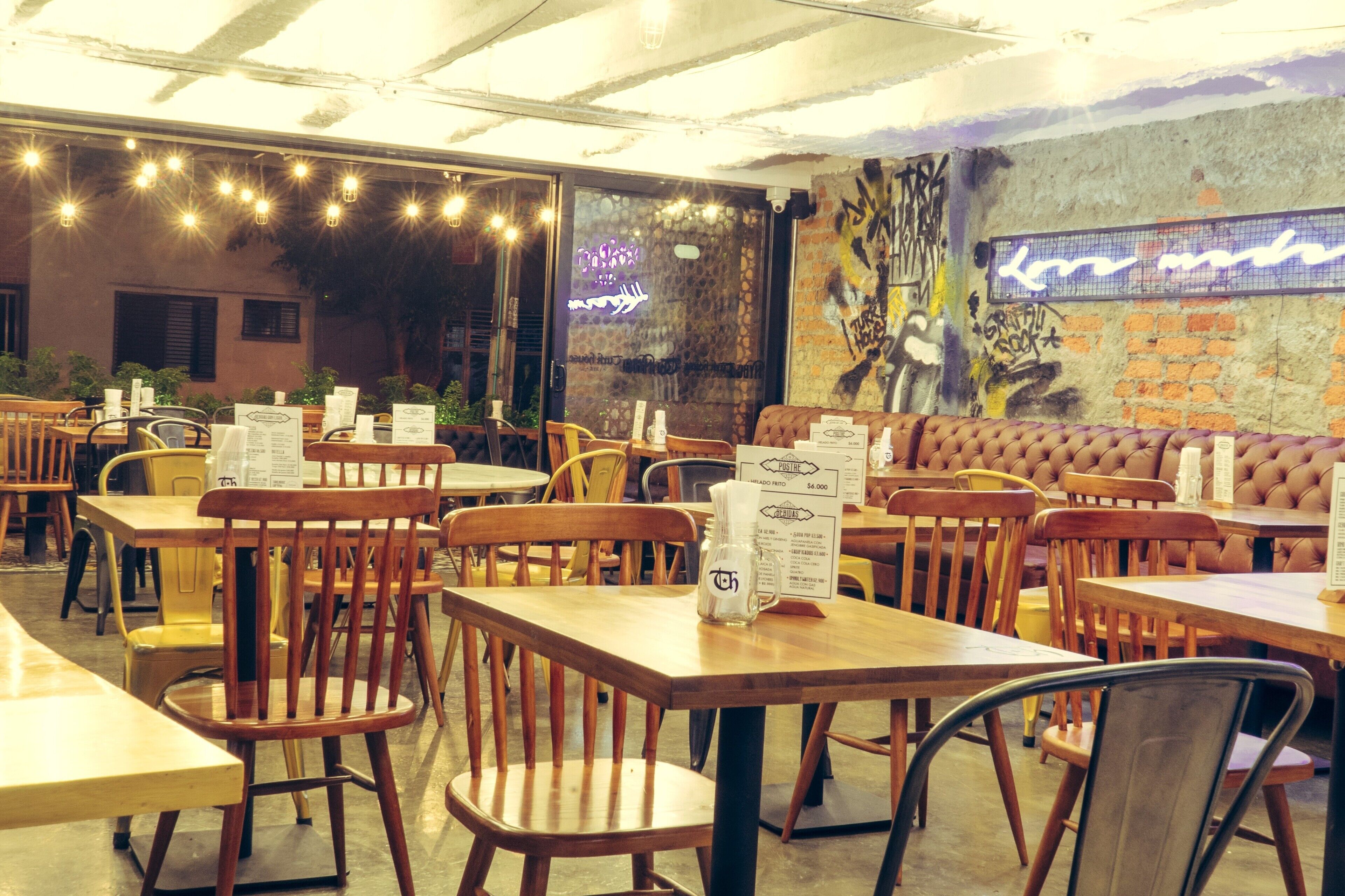 A restaurant with wooden tables and chairs, a neon sign, and a graffiti wall.