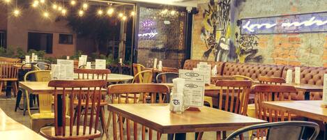 A restaurant with wooden tables and chairs, a neon sign, and a graffiti wall.