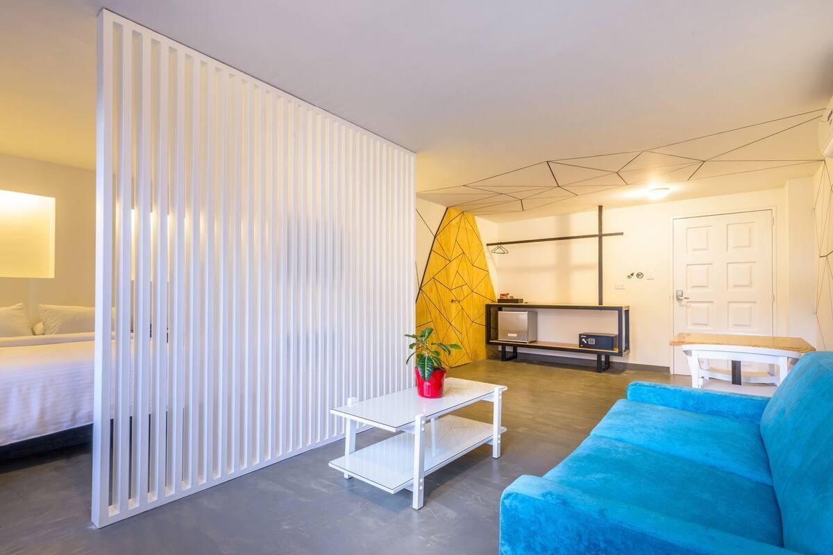 A modern hotel room with a bed, a sofa, a TV, and a partition wall.