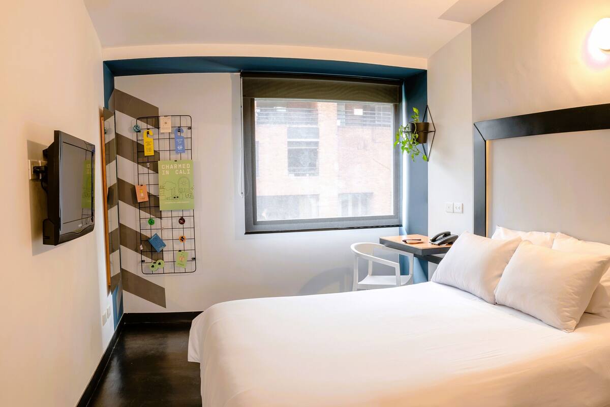 A hotel room with a bed, a desk, a chair, a window, and a wall-mounted TV.
