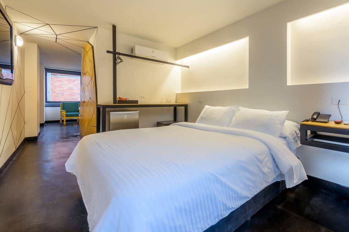 A modern hotel room with a large bed, a desk with a chair, and a view of the outside.