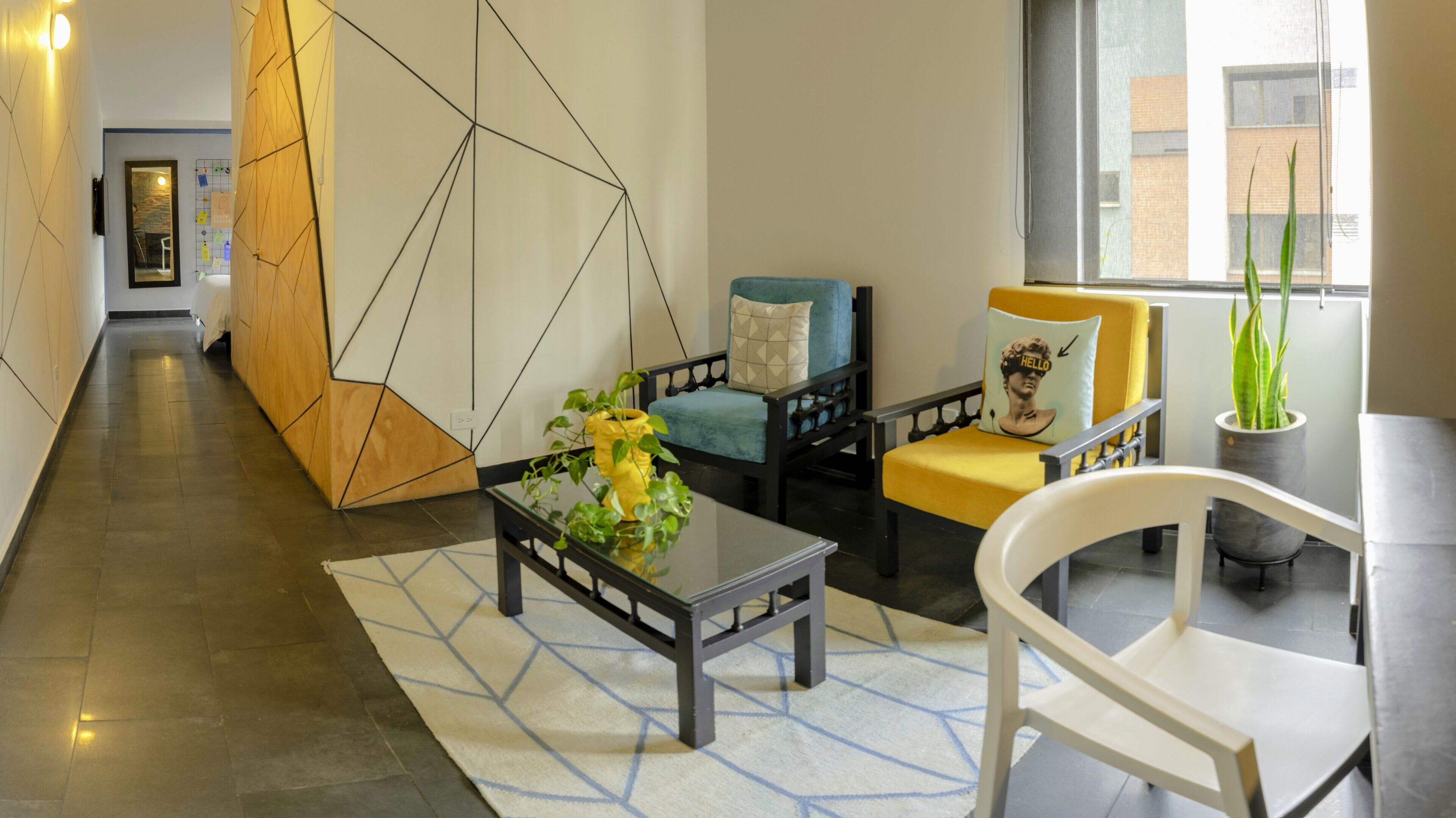 En moderne lobby med et geometrisk vægdesign, et sofabord med planter og siddeområder med puder.