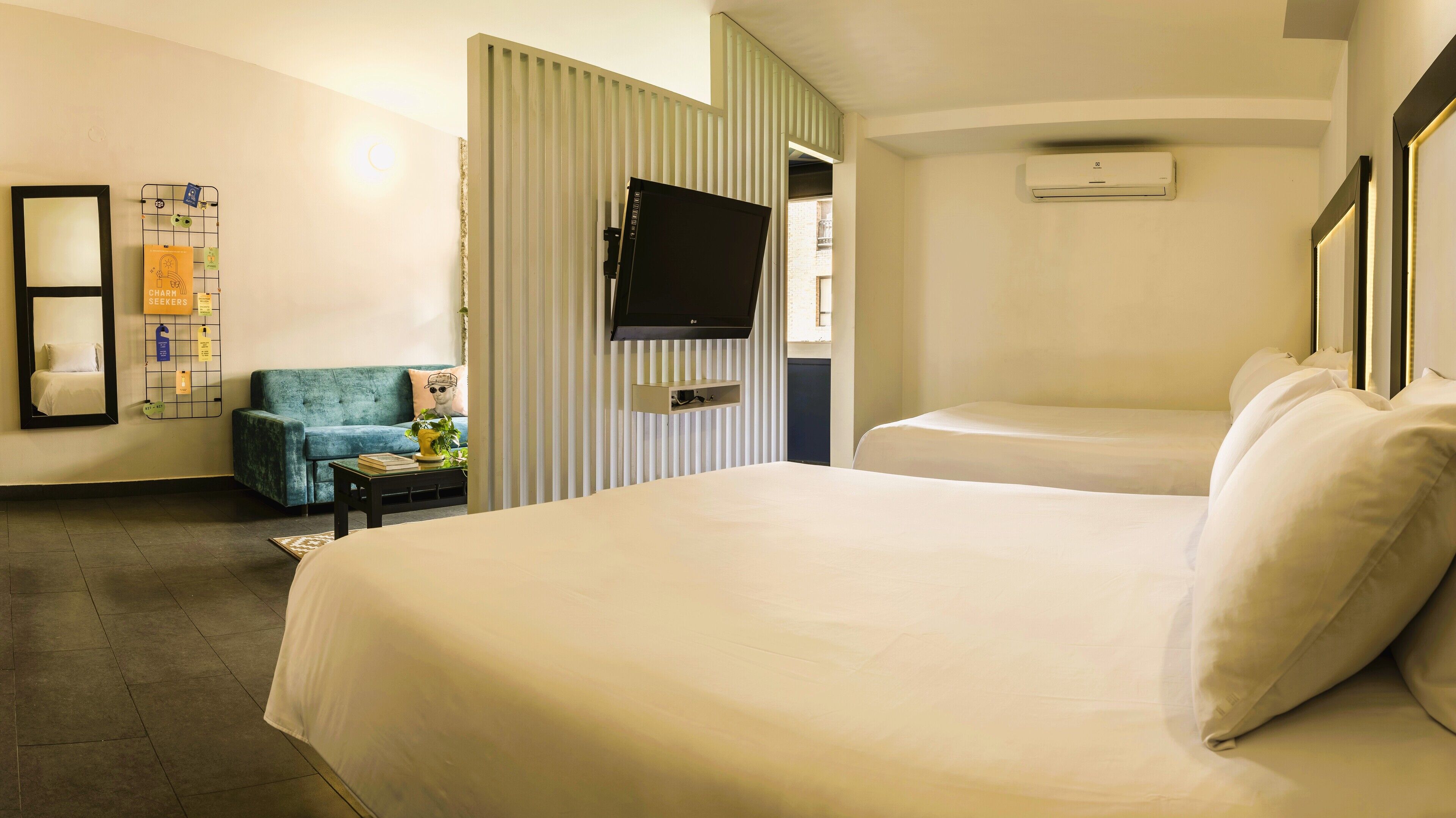 A hotel room with a large bed, a small sofa, a TV mounted on the wall, and a window with blinds.