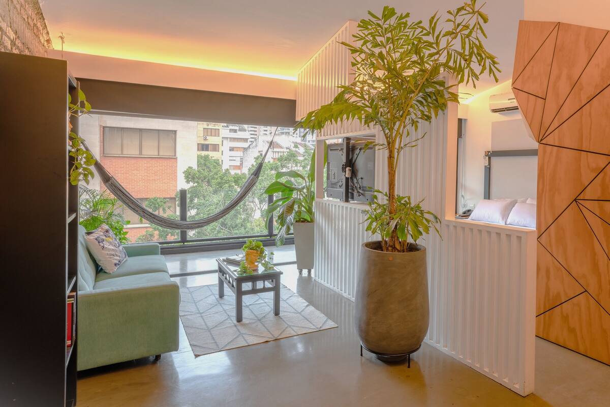 A modern living room with a hammock, a large potted plant, a sofa, and a coffee table.