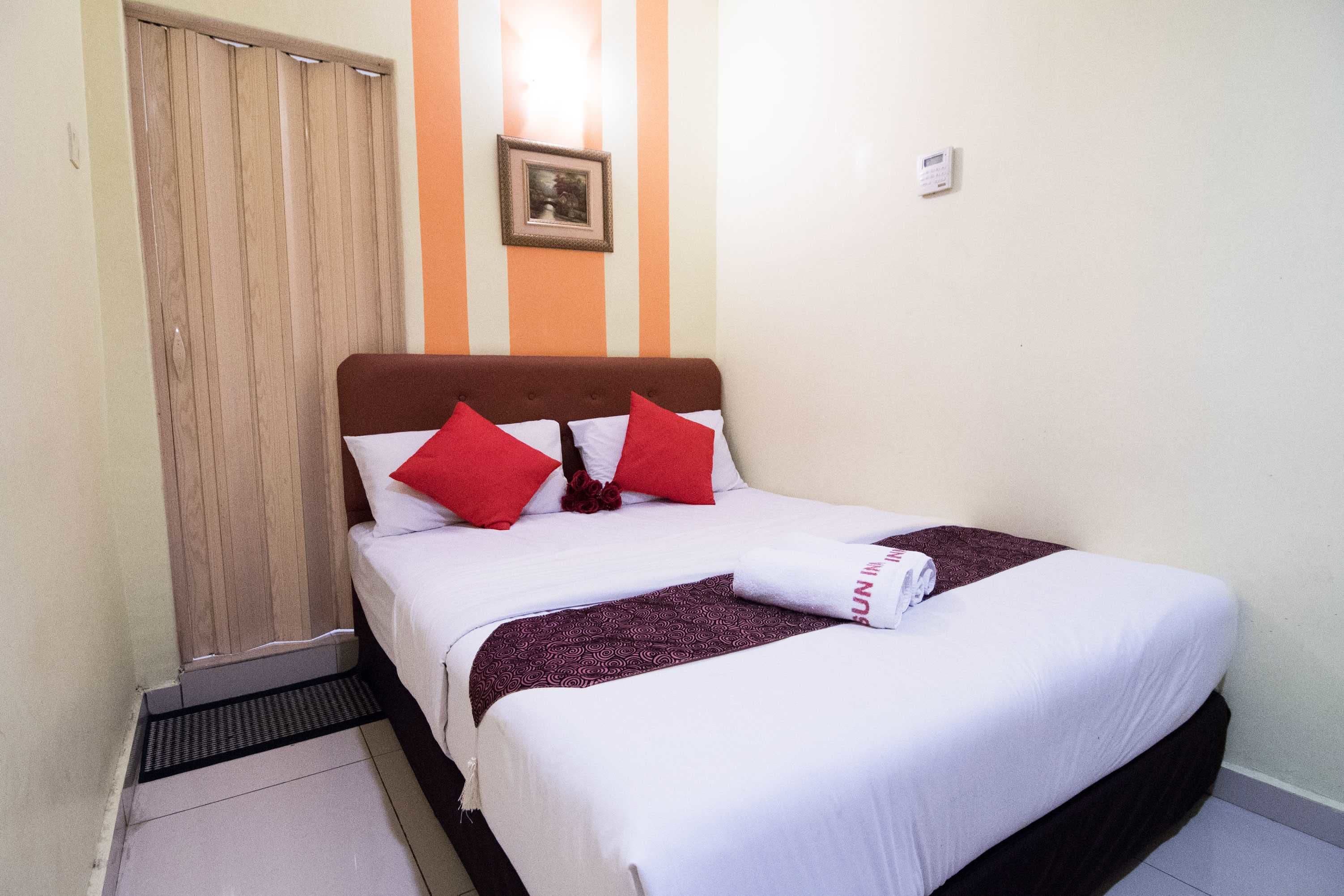 A neatly made bed with white and red bedding, a brown headboard, and a framed picture on the wall.