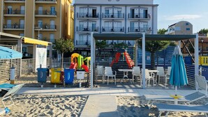 Ett område vid stranden med en pool, solstolar och en byggnad med balkonger.