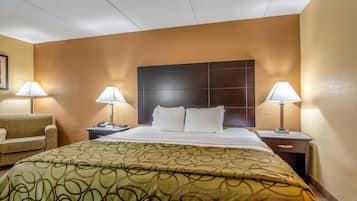 A hotel room with a large bed, two bedside tables with lamps, a sofa, and a headboard with a dark panel.