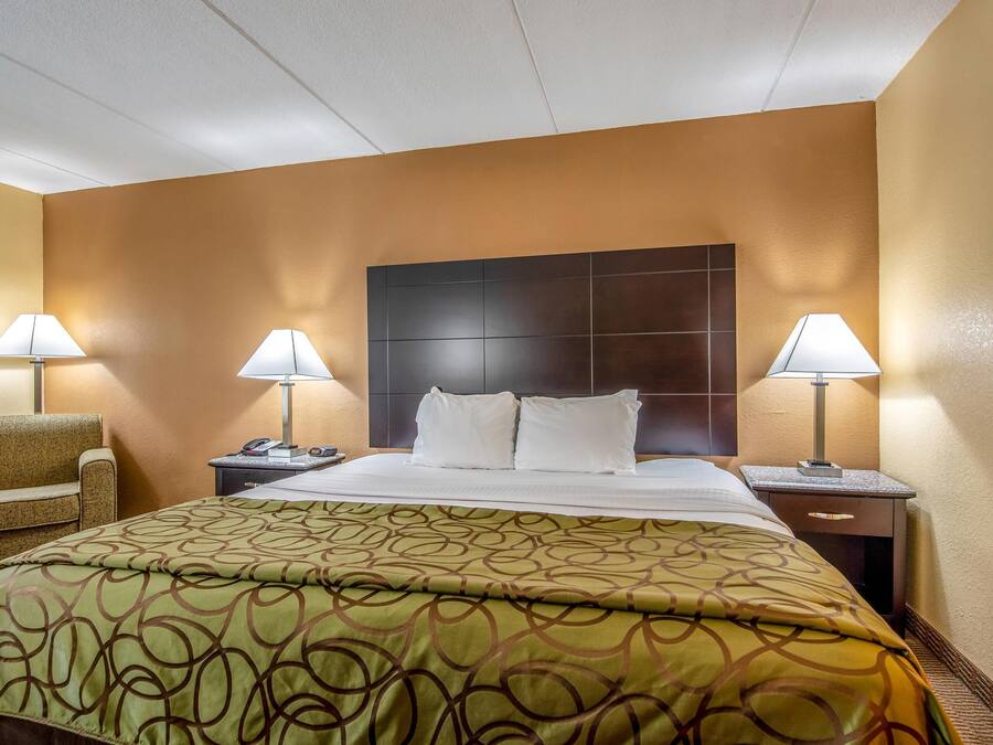 A hotel room with a large bed, two bedside tables with lamps, a sofa, and a headboard with a dark panel.