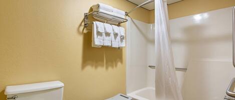 Un baño con inodoro, ducha con cortina, toallero con toallas y un taburete pequeño.