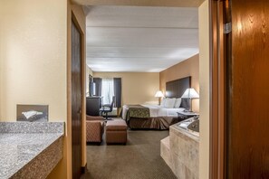 A hotel room with a bed, a desk, a chair, a small table, and a bathroom area. - Quality Inn Tully I-81 (Tully)